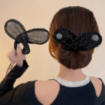 A woman with her back to the camera models a black mesh rabbit ear headband featuring white polka dots and sparkling silver circular embellishments. She holds a second, similar headband in her hand.